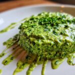A thick dollop of vibrant green cilantro lime sauce, topped with fresh herbs, dripping down a white plate.