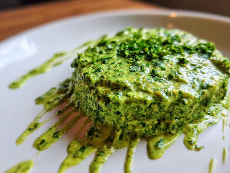 A thick dollop of vibrant green cilantro lime sauce, topped with fresh herbs, dripping down a white plate.