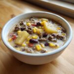 Close-up of a white bowl filled with creamy cowboy soup containing ground beef, potatoes, corn, and kidney beans.