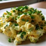 A mound of creamy, yellow egg salad recipe generously topped with bright green chopped chives on a white plate.