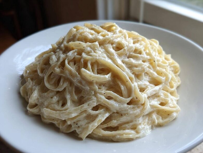 A close-up of fettuccine pasta generously coated in rich, creamy homemade alfredo sauce, served on a white plate.