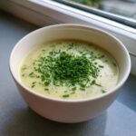 A white bowl filled with creamy potato leek soup, garnished generously with freshly chopped green chives.