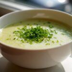 A close-up of a bowl of creamy potato leek soup garnished generously with bright green chopped chives.