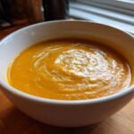 Close-up of a bowl of vibrant orange, creamy pumpkin soup swirled with cream.