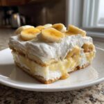 A thick, creamy slice of banana pudding layered with wafers, pudding, and topped with whipped cream and fresh banana slices.