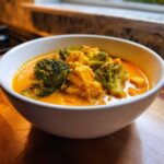 A close-up of creamy vegan pumpkin curry featuring bright green broccoli florets and tofu chunks in a white bowl.