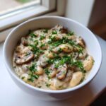 A close-up of creamy white bean mushroom stew served in a white bowl, topped generously with fresh chopped parsley.