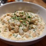 Close-up of a white bowl filled with creamy white chicken chili recipe, featuring shredded chicken and white beans.