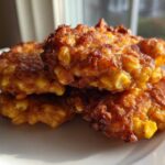 Close-up of three golden brown, crispy corn fritters stacked on a white plate, highlighting the visible corn kernels.