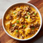 A close-up of a bowl of rich crockpot cheeseburger soup topped with ground beef, melted cheddar cheese, and green onions.