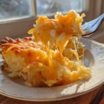 A fork lifts a cheesy, stringy bite of crockpot cheesy potatoes with a golden-brown top.