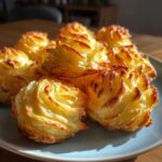 A close-up of several golden-brown, piped duchess potatoes arranged on a light blue plate.