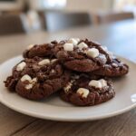 A stack of rich, dark chocolate hot chocolate cookies topped with melted chocolate chips and mini marshmallows.