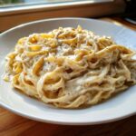 A close-up of fettuccine pasta generously coated in creamy homemade alfredo sauce and sprinkled with black pepper.