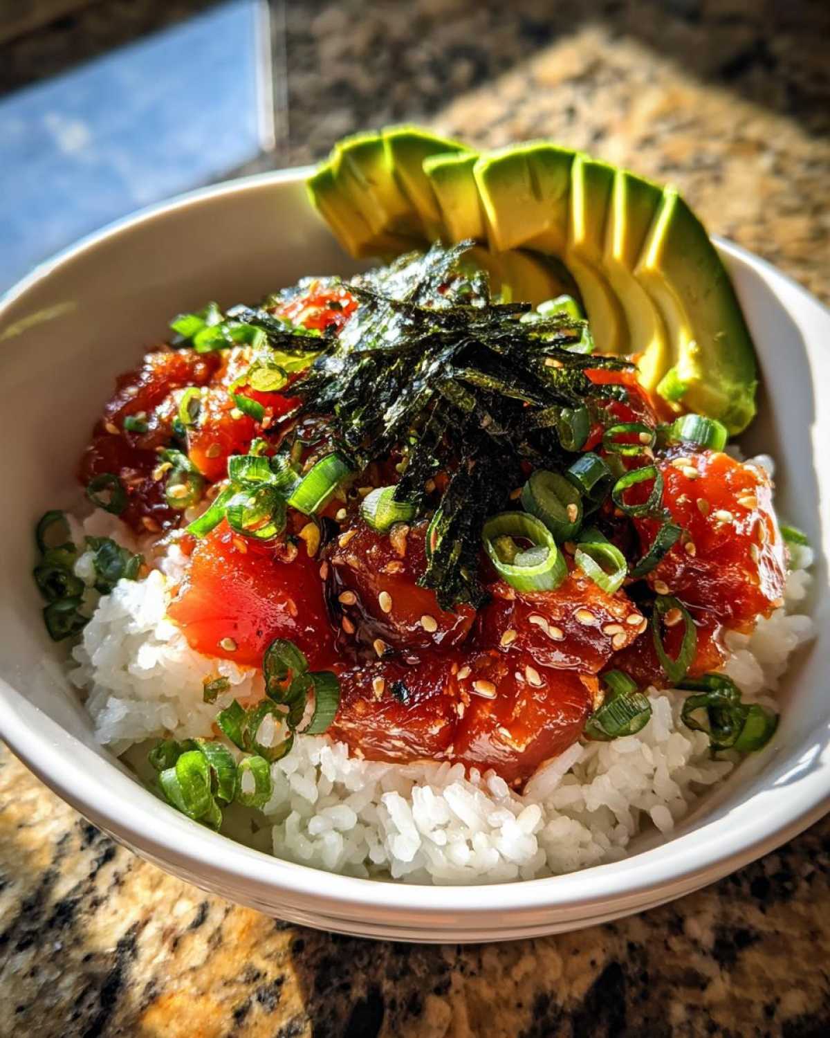 Close-up of a flavorful tuna rice bowl topped with marinated tuna, sliced avocado, nori, and green onions.