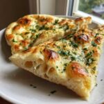 Close-up of fluffy, golden-brown naan bread slices brushed with garlic butter and topped with fresh parsley.