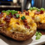 Two fluffy twice baked potatoes loaded with melted cheddar cheese, bacon bits, and green onions.