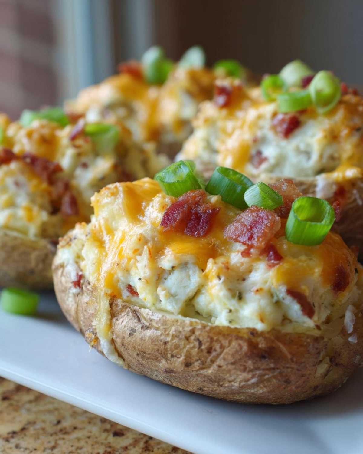 Close-up of fluffy twice baked potatoes stuffed with filling, topped with melted cheddar cheese, bacon bits, and green onions.