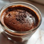 Close-up of rich, airy chocolate mousse topped with shavings in a clear glass.