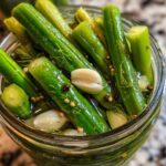 Close-up overhead shot of bright green dilly beans packed tightly in a glass jar with garlic cloves, dill sprigs, and pickling spices.
