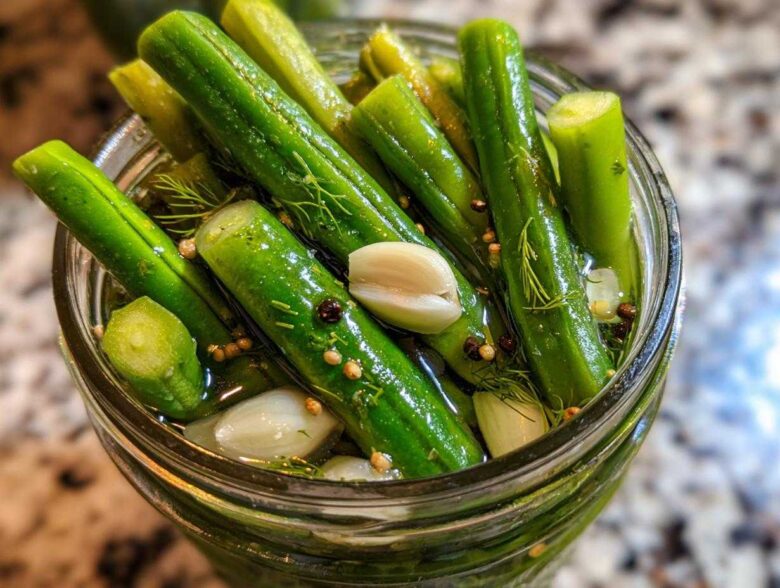 Close-up overhead shot of bright green dilly beans packed tightly in a glass jar with garlic cloves, dill sprigs, and pickling spices.