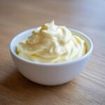 A close-up of thick, creamy homemade mayonnaise swirled high in a small white bowl.