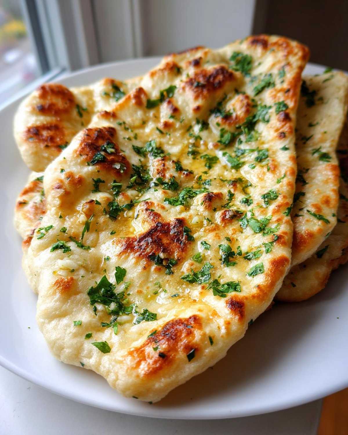 Close-up of freshly baked naan bread brushed with melted butter, garlic, and chopped parsley.
