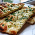 Close-up of three slices of fluffy, charred naan bread brushed with melted butter, garlic, and fresh parsley.