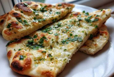 Close-up of three slices of fluffy, charred naan bread brushed with melted butter, garlic, and fresh parsley.