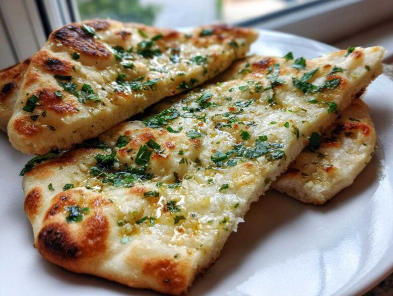 Close-up of three slices of fluffy, charred naan bread brushed with melted butter, garlic, and fresh parsley.