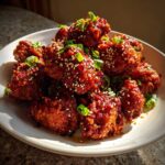 A pile of crispy, glazed korean fried chicken recipe pieces topped with sesame seeds and chopped green onions.
