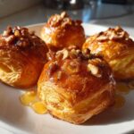Four golden, flaky pastries topped with honey glaze and chopped nuts, resembling goat cheese and honey bites.