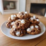 A tempting stack of freshly baked hot chocolate cookies topped with melted marshmallows and chocolate chips.
