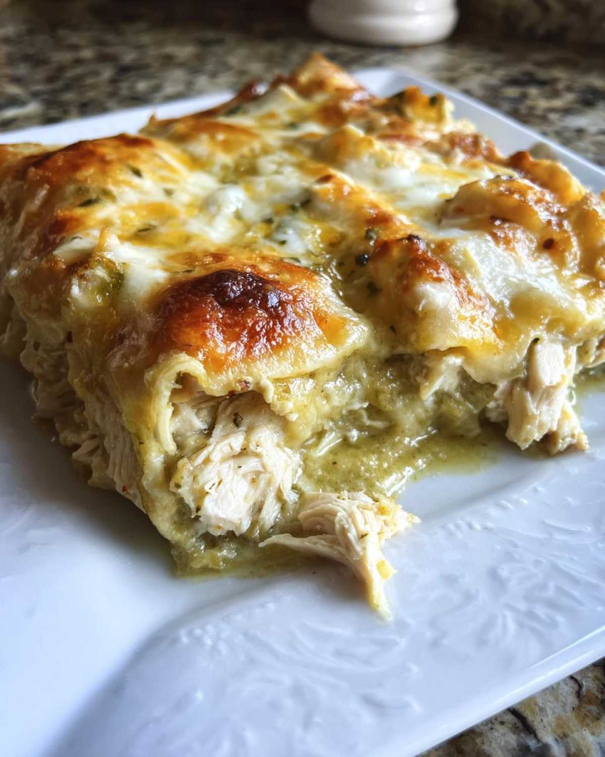 A close-up of a serving of green chile chicken enchiladas showing shredded chicken and melted, browned cheese.