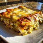 Close-up of cheesy green chile chicken enchiladas with shredded chicken filling visible.