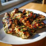 Close-up of grilled chicken pieces coated in a vibrant herb chicken marinade, served on a white plate.