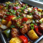 Close-up of glistening, glazed Hawaiian chicken sheet pan with pineapple, peppers, and green onions.