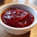 Close-up of rich, dark red homemade bbq sauce served in a small white dipping bowl.