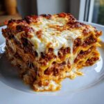 A thick, towering slice of homemade lasagna featuring layers of pasta, rich meat sauce, and gooey, melted cheese topping.
