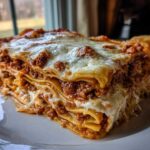 A thick, layered slice of homemade lasagna featuring rich meat sauce and melted mozzarella cheese on a white plate.