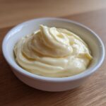 A close-up of freshly made, creamy homemade mayonnaise swirled beautifully in a small white ramekin.