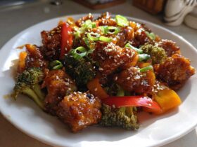 Close-up of glossy honey garlic chicken stir fry with broccoli florets, peppers, and sesame seeds.