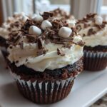 Close-up of rich chocolate hot chocolate cupcakes topped with white frosting, chocolate shavings, and mini marshmallows.