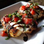 Close-up of two servings of juicy caprese chicken topped with melted mozzarella, diced tomatoes, fresh basil, and balsamic glaze.