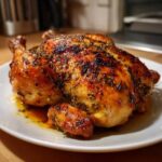 A whole, perfectly roasted spatchcock chicken with golden-brown, herb-crusted skin resting on a white plate.