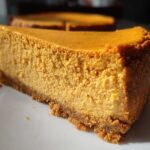 A thick slice of creamy keto pumpkin cheesecake with a graham-style crust, sitting on a white plate.