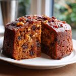 Close-up of a moist fruit cake, cut in half, showing rich texture packed with raisins and walnuts.