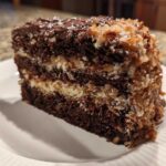 A tall slice of moist german chocolate cake recipe showing dark chocolate layers and thick coconut pecan frosting.