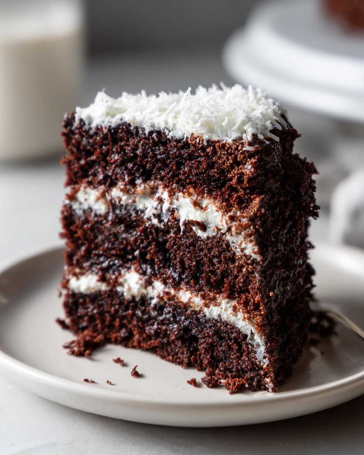 Close-up of a decadent slice of german chocolate cake recipe showing three layers of dark chocolate cake and white coconut-pecan frosting.