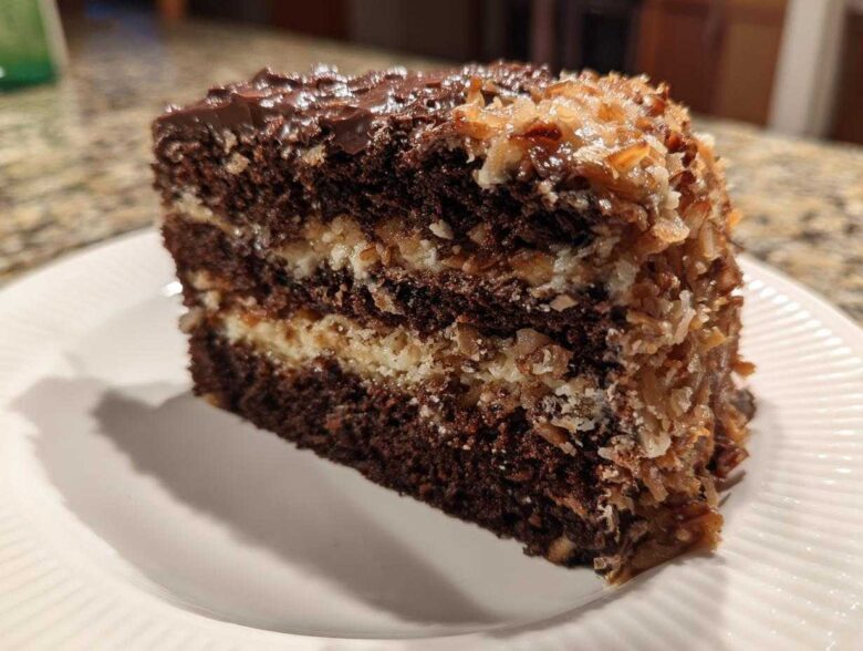 A tall slice of moist german chocolate cake recipe showing dark chocolate layers and thick coconut pecan frosting.